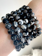 Side view of multiple Orca Agate bracelets stacked on wrist, showing bold black-and-white banded patterns with subtle gray marbling in polished round beads