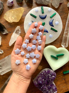 Blue Lace Agate stars on a hand, shown with a crystal grid & assorted crystals on a wood table — tools for peaceful, intentional energy work