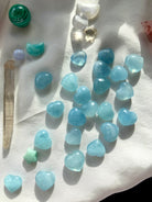 Wide angle of Aquamarine hearts with mini crystals + quartz point on white silk — calming crystal hearts for intention setting + chakra work.