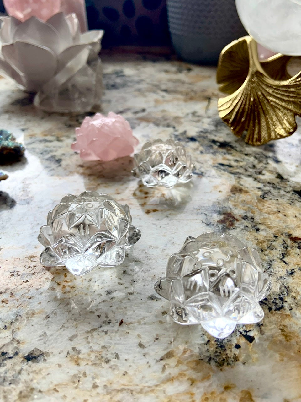 Carved clear quartz crystal lotus flowers displayed on a surface with other crystals.