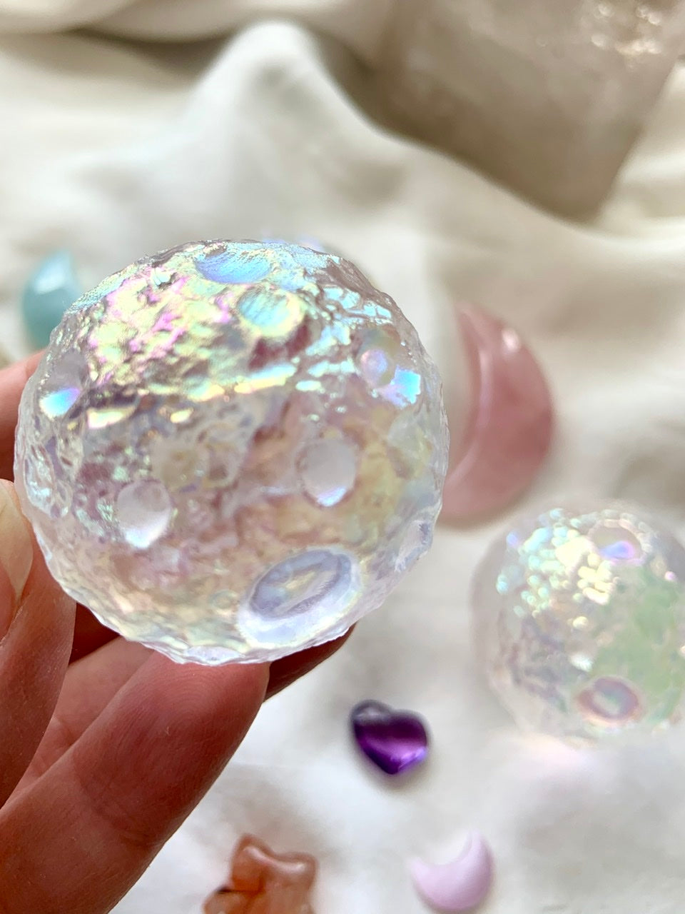 Close-up of Angel Aura Full Moon sphere with soft crystal background on white silk — glowing lunar texture with ethereal rainbow sheen.