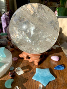 A huge clear quartz sphere safely displayed on a wood crystal holder shown in a crystal collection