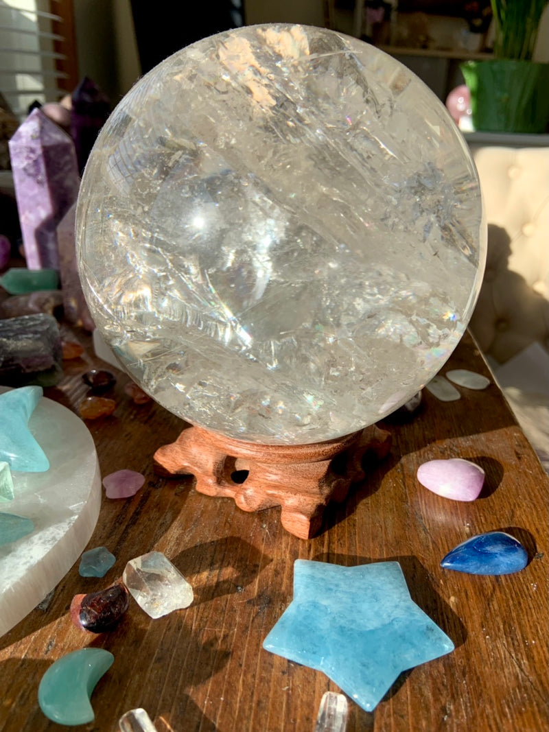 A huge clear quartz sphere safely displayed on a wood crystal holder shown in a crystal collection