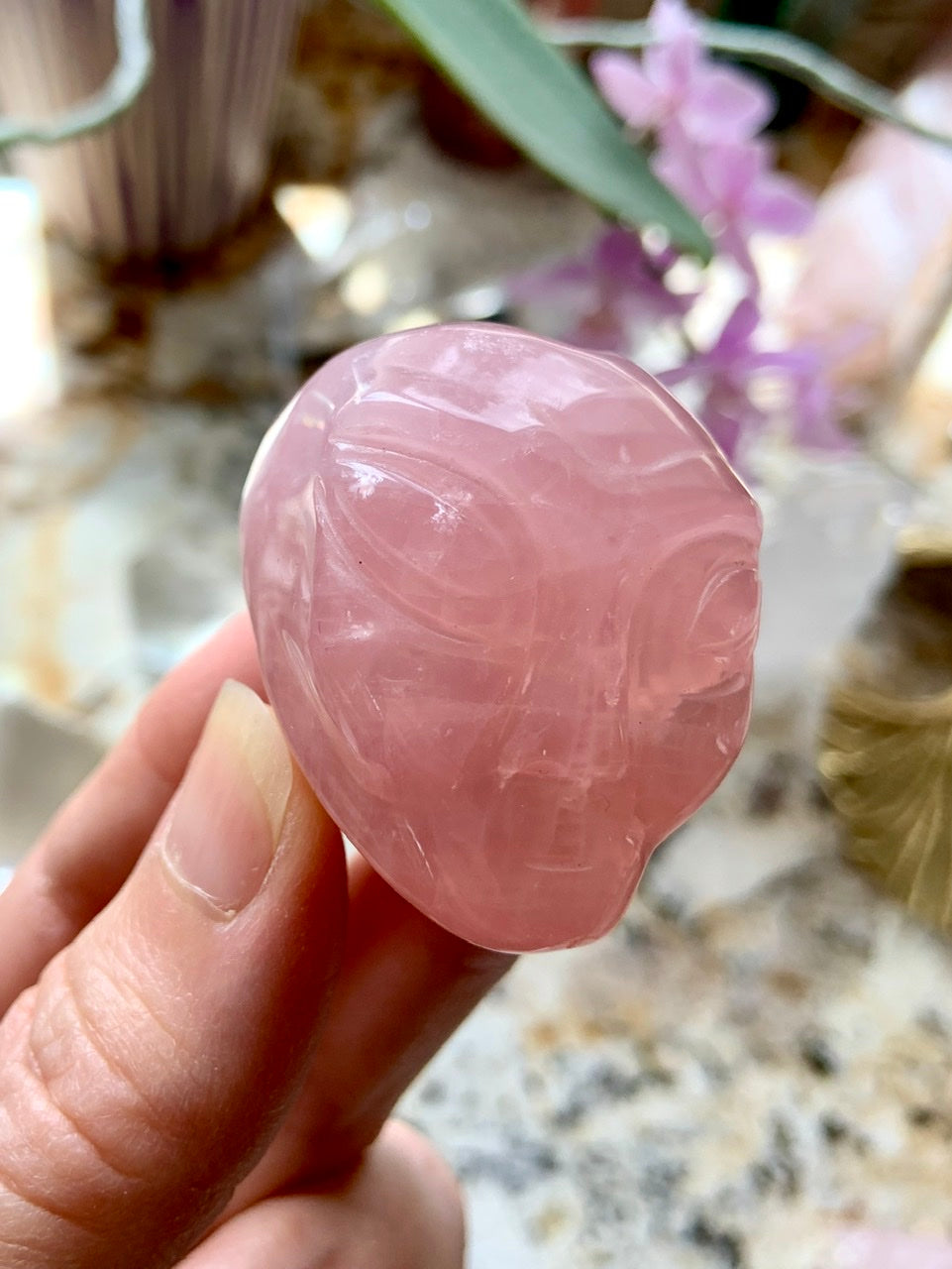 Close-up of one Rose Quartz alien head in hand, carved crystal skull with gentle pink color and galactic alien features