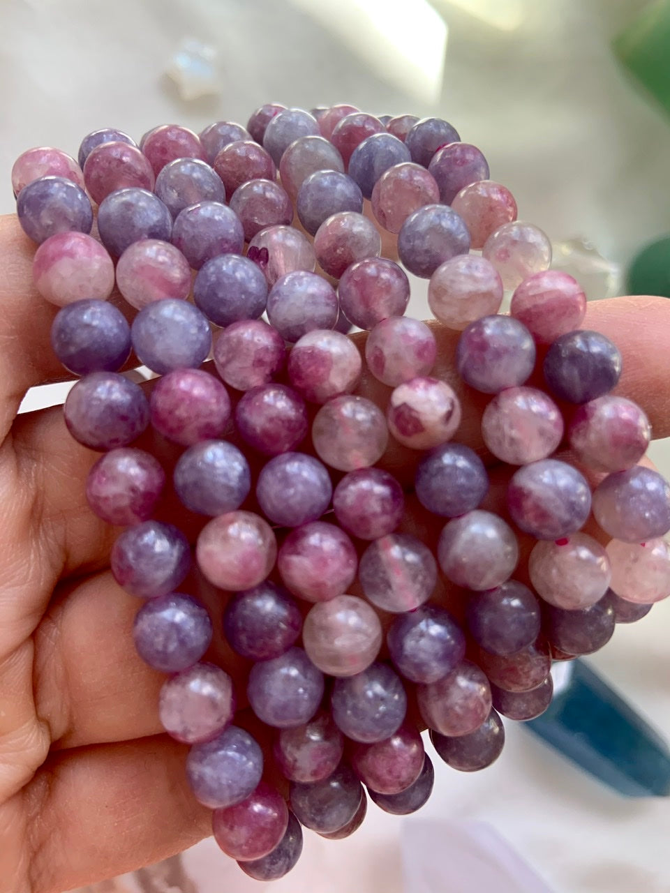 Closeup of Unicorn Stone crystal bracelets held on a hand — high quality pink and purple beads with Pink Tourmaline in Lepidolite for heart chakra healing.