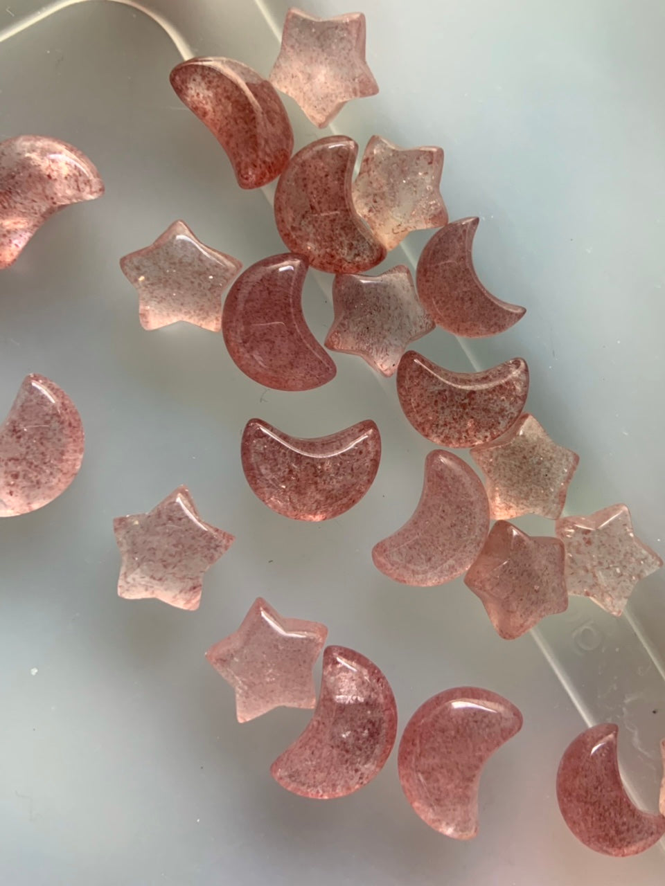 Closeup of Strawberry Quartz moons and stars on translucent white background — showcasing the high-quality clarity and rich tanzberry hues