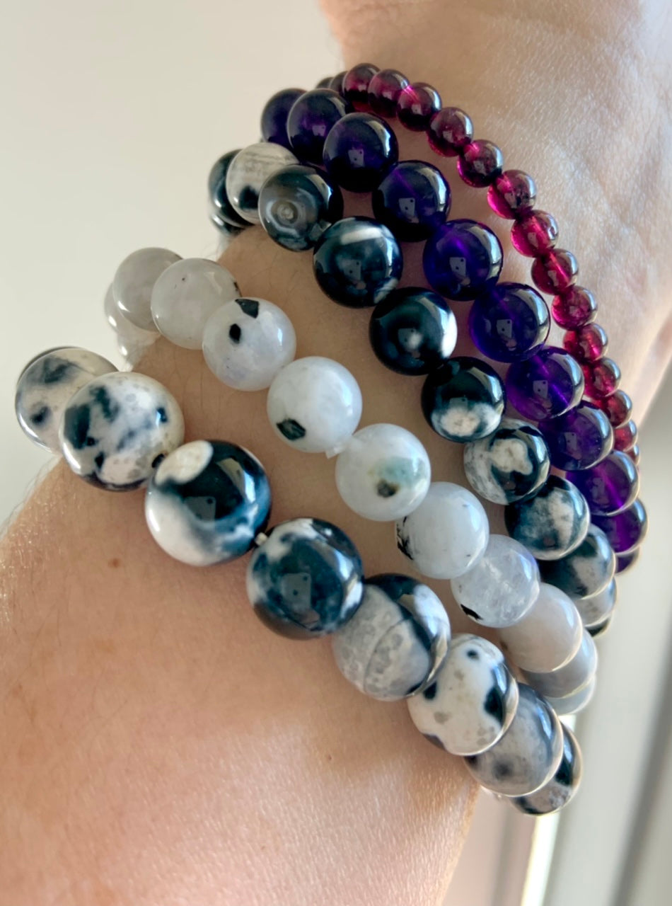 Stack of healing crystal bracelets featuring Orca Agate, Rainbow Moonstone, Amethyst, and Garnet for chakra alignment and emotional healing