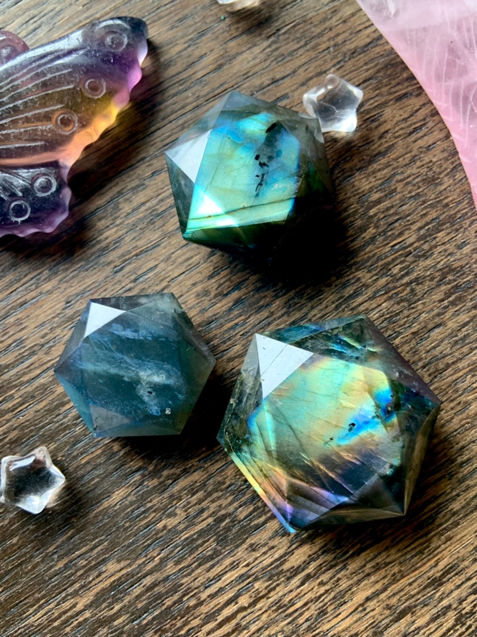 Flashy faceted Labradorite hexagon crystals in deep blue, teal & rainbow tones on dark wood with clear quartz stars — powerful crystals for intuition, clarity & protection.