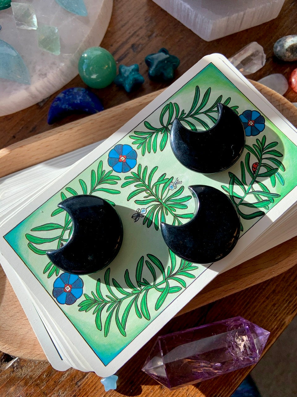 Set of three Black Obsidian crescent moons on a stack of tarot cards beside an amethyst Vogel — crystals for protection, intuition & spiritual balance