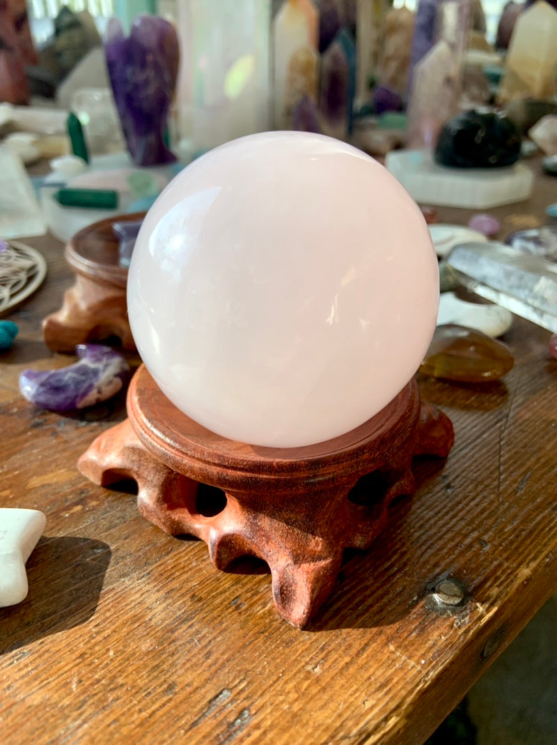 pink mangano calcite sphere on a wood stand