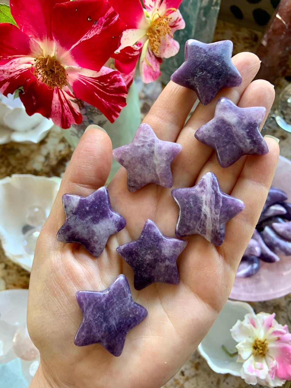 Purple Lepidolite Star shaped crystal carvings shown on my hand for scale with a blooming rose 