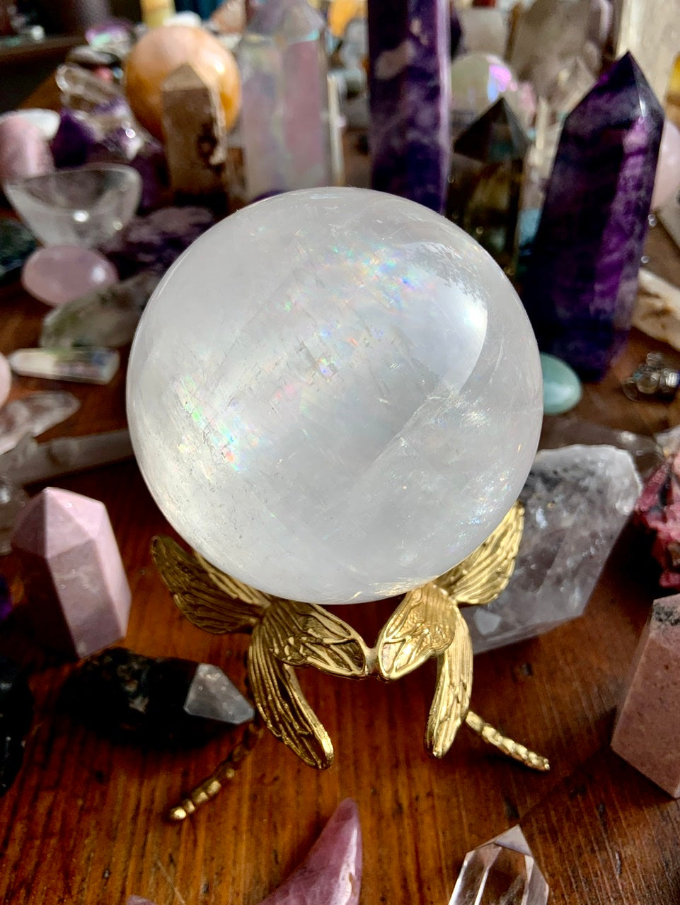 Angled view of gold dragonfly crystal stand displaying an optical calcite sphere in a colorful crystal collection.