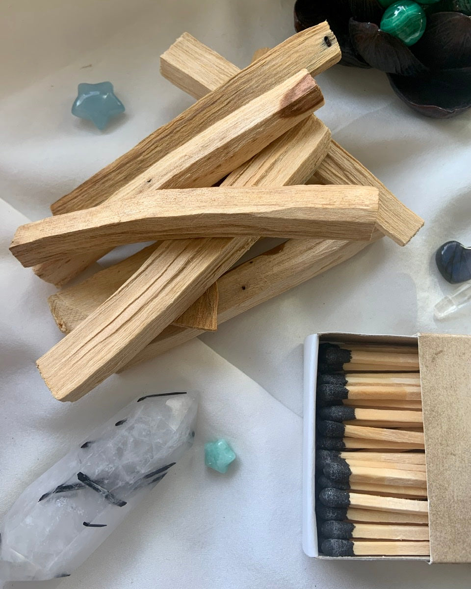 Flatlay of Palo Santo sticks, matchbox, and healing crystals – altar tools for spiritual cleansing and sacred space rituals