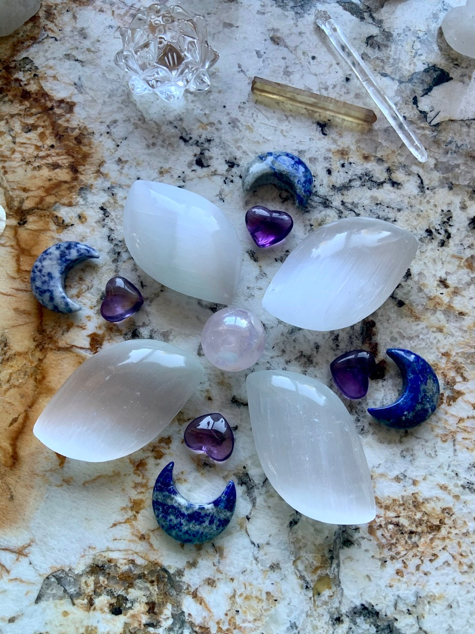 Flower-shaped crystal grid with selenite petals, Lapis Lazuli moons, and Aura Rose Quartz centerpiece — sacred layout for spiritual alignment