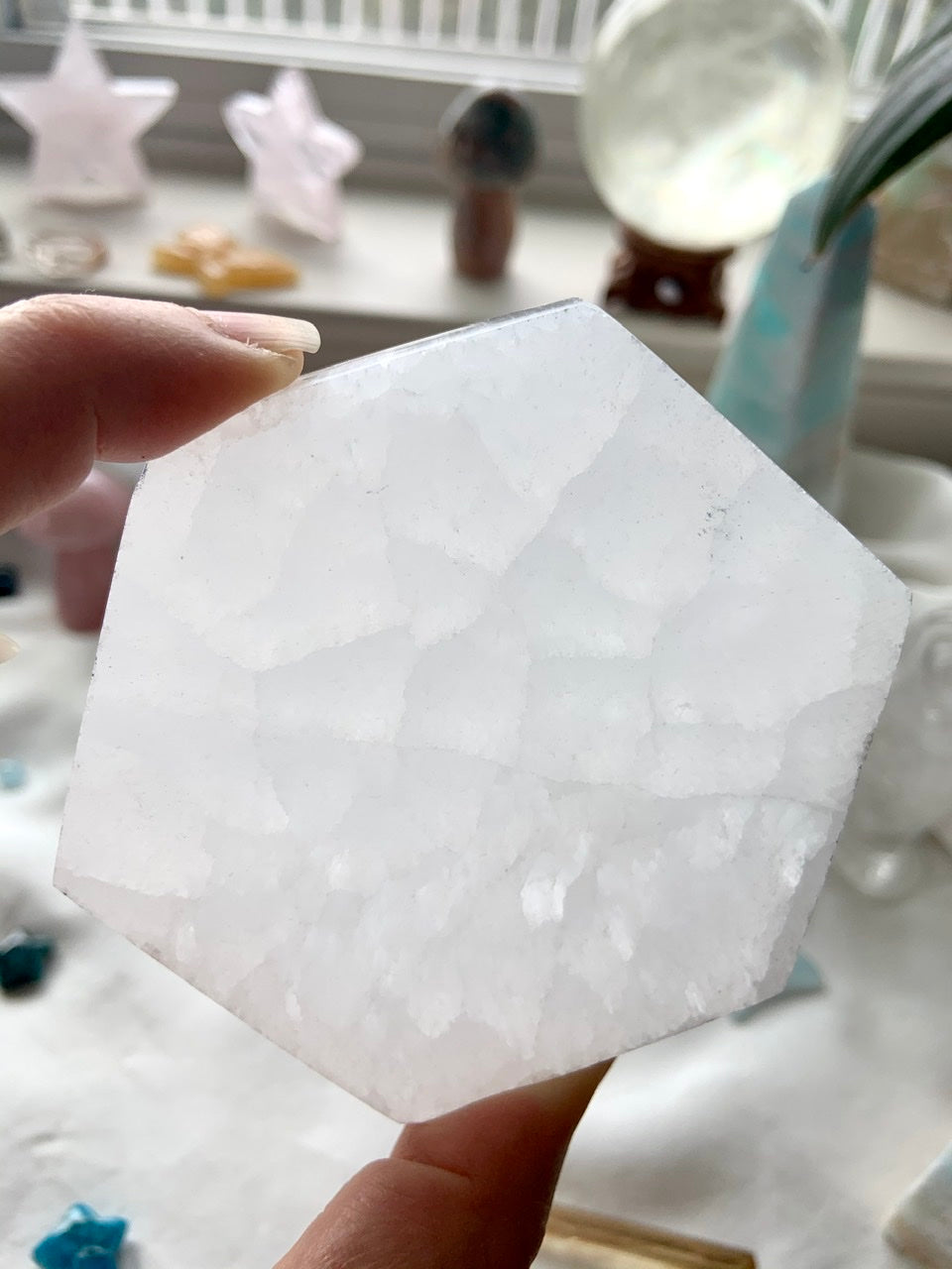 Closeup of a Selenite Hexagon Charging Plate held to the light, showing natural glow, translucence, & pattern in the stone