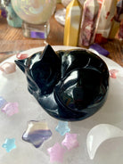 Black Obsidian Sleeping Cat Carving shown on a selenite plate surrounded by with celestial crystals
