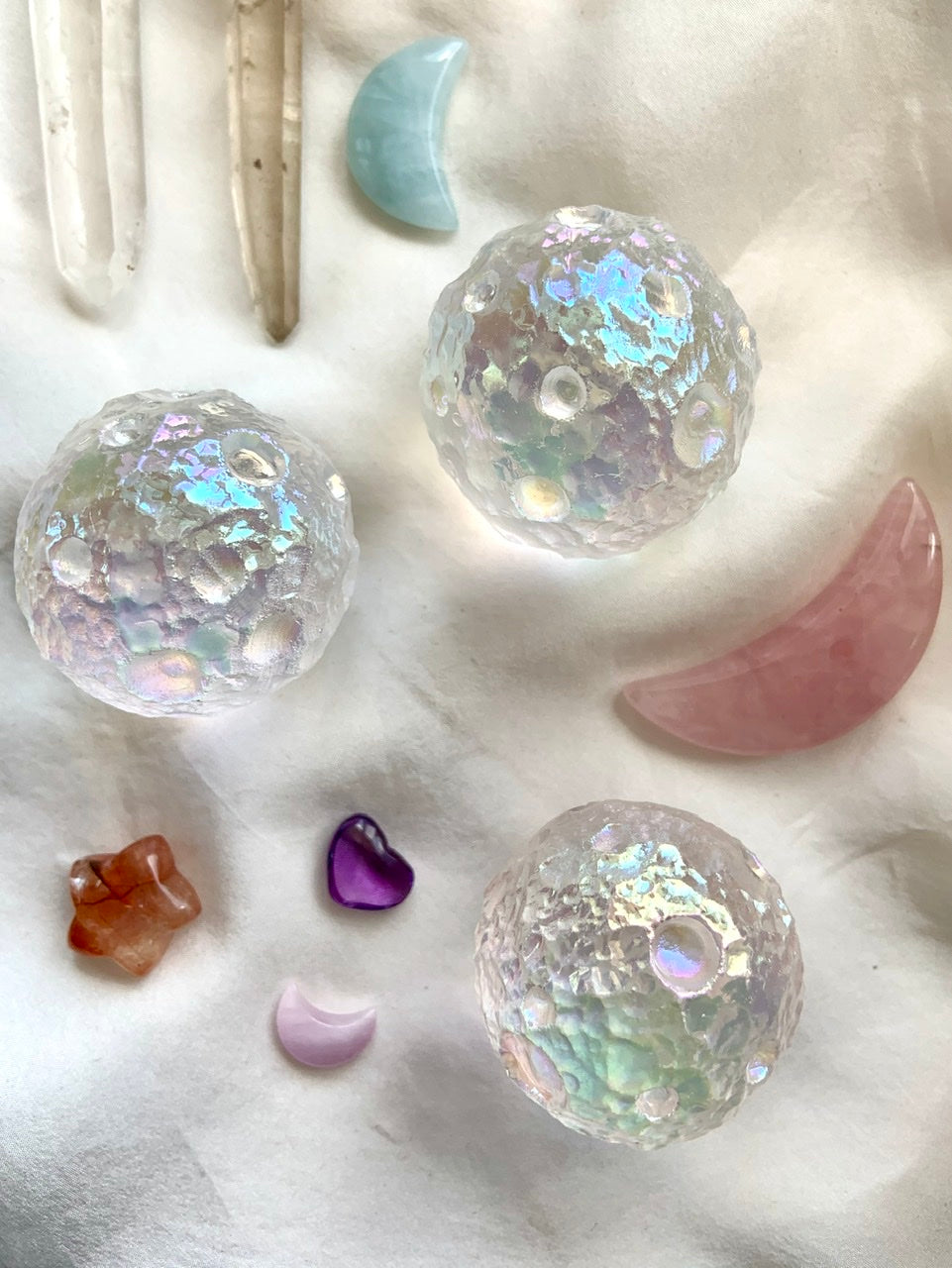 Angel Aura Full Moon crystal spheres arranged with cosmic crystals — rose quartz moon, aquamarine moon, quartz points — on soft white silk for dreamy display.