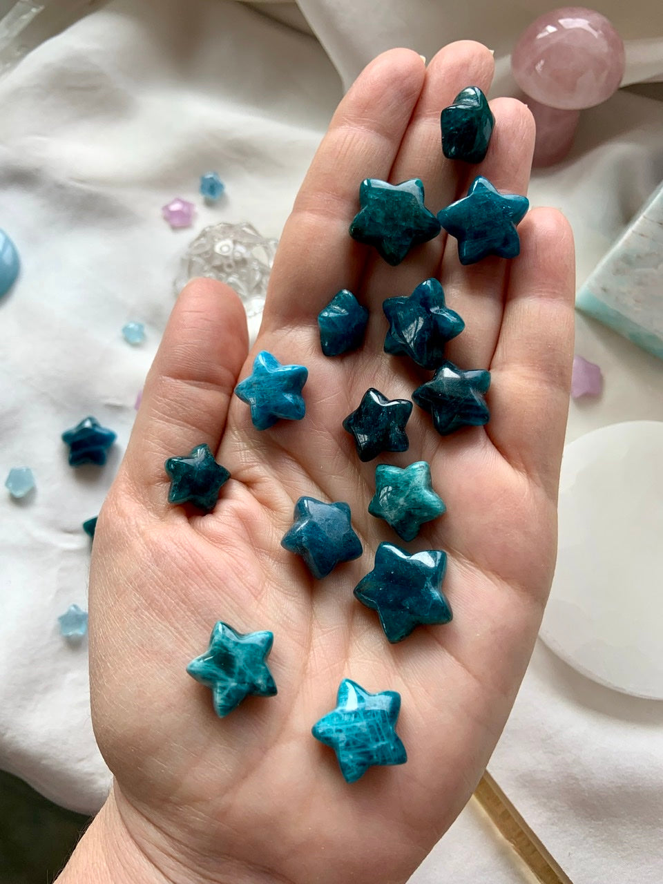 Mini Blue Apatite crystal stars shown on hand for scale — teal carved stars for communication, clarity & Throat Chakra expression.
