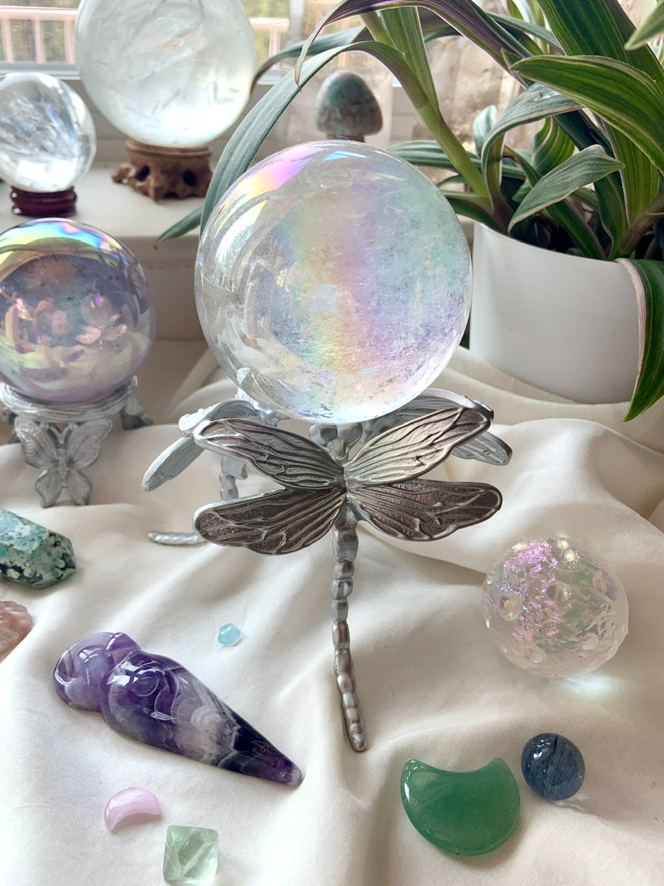 Alternate view of silver dragonfly crystal holder with angel aura quartz sphere and assorted crystals on white silk.