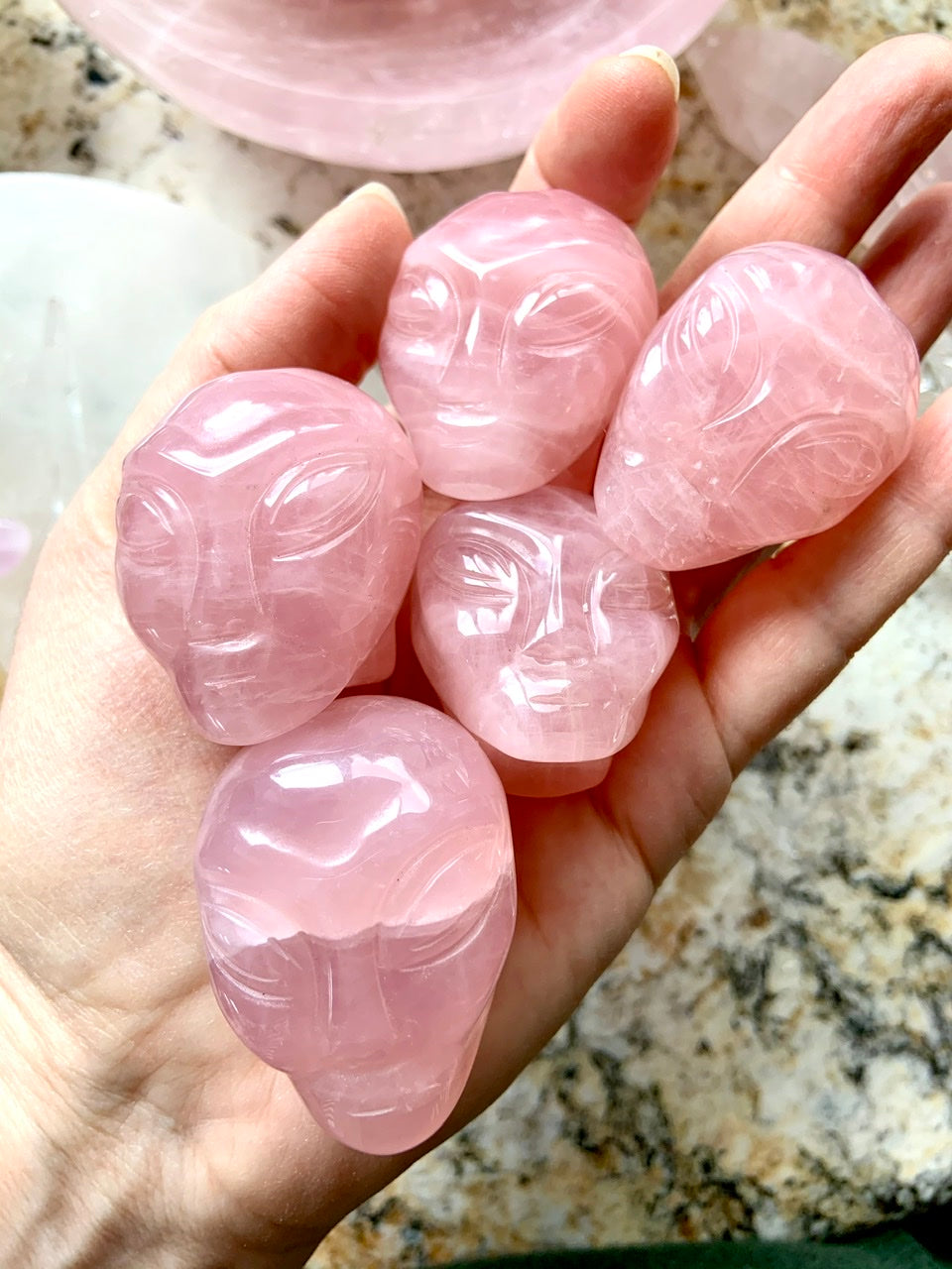 Group of five pink Rose Quartz alien face carvings with high polish, displayed on open palm