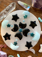 Overhead crystal grid with Blue Apatite stars, aquamarine moons & obsidian carvings — arranged on a white selenite plate with dreamy crystals for energy alignment.