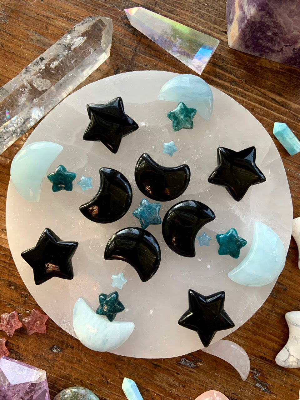 Overhead crystal grid with Blue Apatite stars, aquamarine moons & obsidian carvings — arranged on a white selenite plate with dreamy crystals for energy alignment.