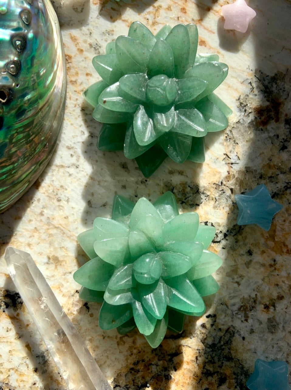 Two Green Aventurine crystal succulent carvings in cactus flower shape displayed on a granite slab with healing crystals for heart chakra energy.