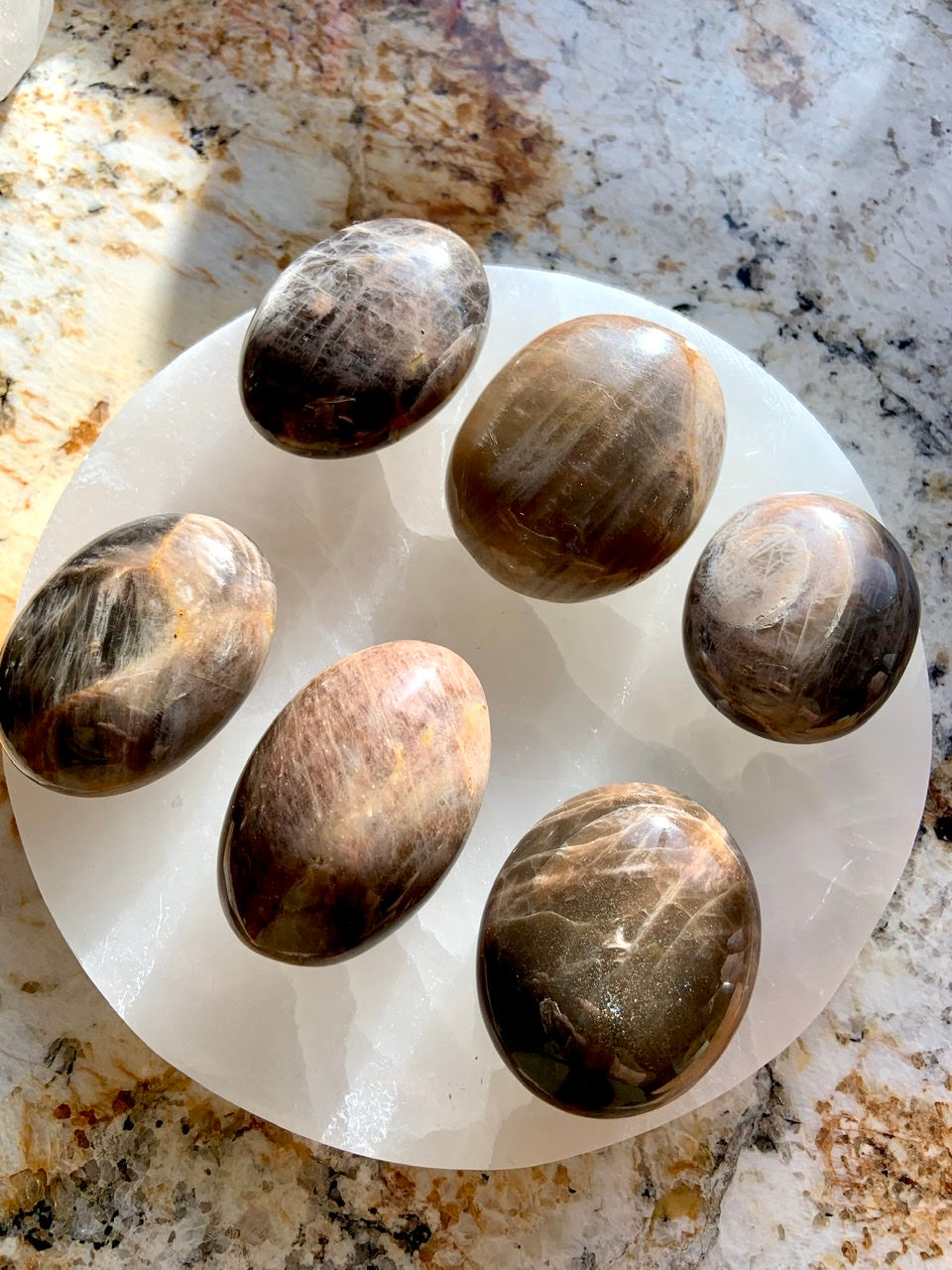 An array of Black Moonstone Palm Stones shown on a white selenite charging plate - crystals for empaths 