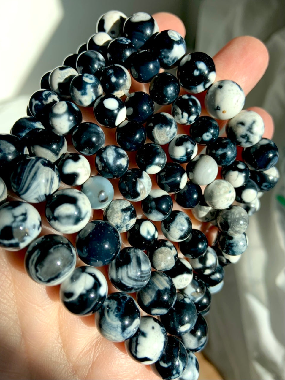Angled closeup of stacked Orca Agate bracelets in mixed bead sizes, highlighting bold black, white, and gray banded patterns