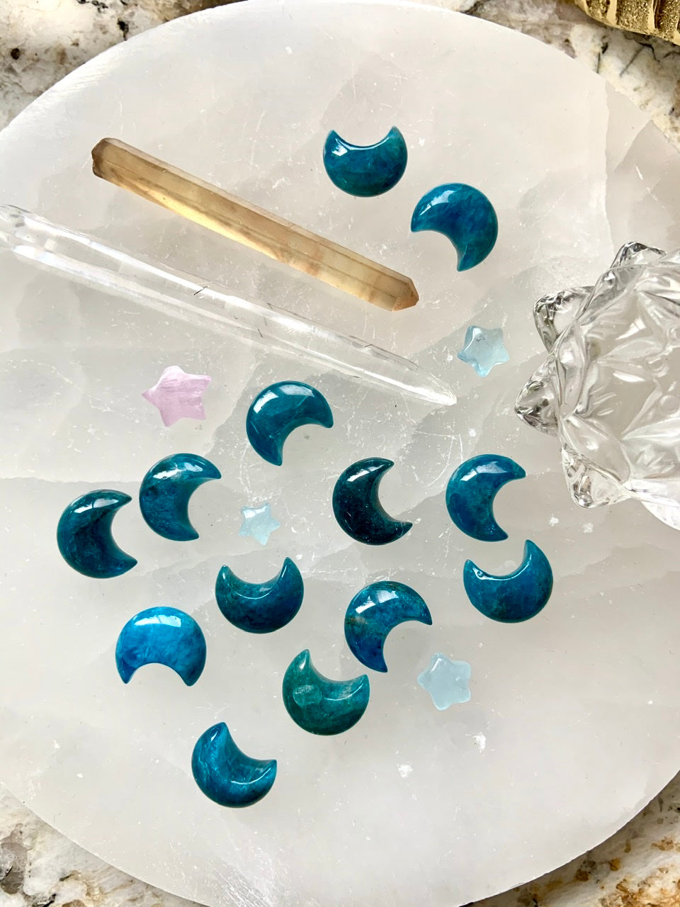 Blue Apatite Crescent Moons on a white selenite plate with quartz points & lotus carving — mini moon crystals for throat chakra clarity & insight.