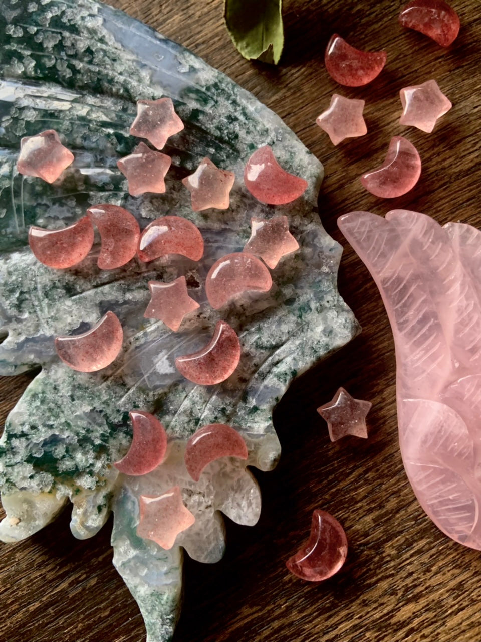 Mini Strawberry Quartz moons and stars arranged on a moss agate wing carving with rose quartz on dark wood — crystal decor for altar or gift giving