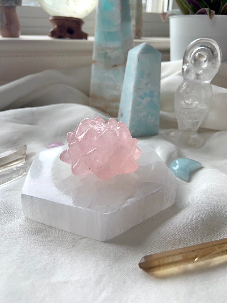 Side view of hexagon selenite plate with rose quartz lotus carving on top, styled with pastel crystal collection