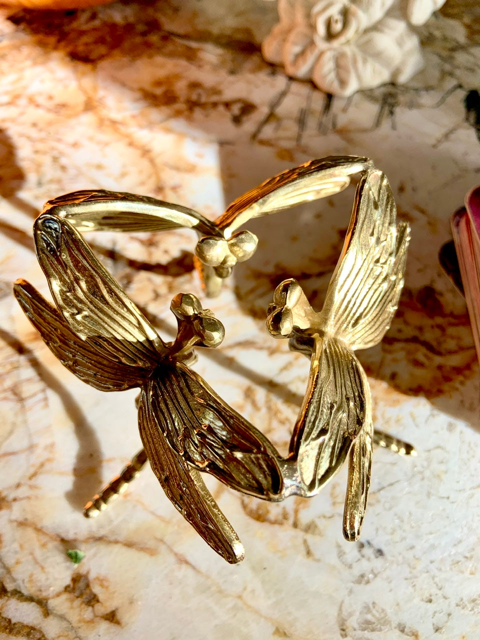 Overhead view of gold dragonfly sphere stand on marble slab — shows intricate wing details of art deco design.