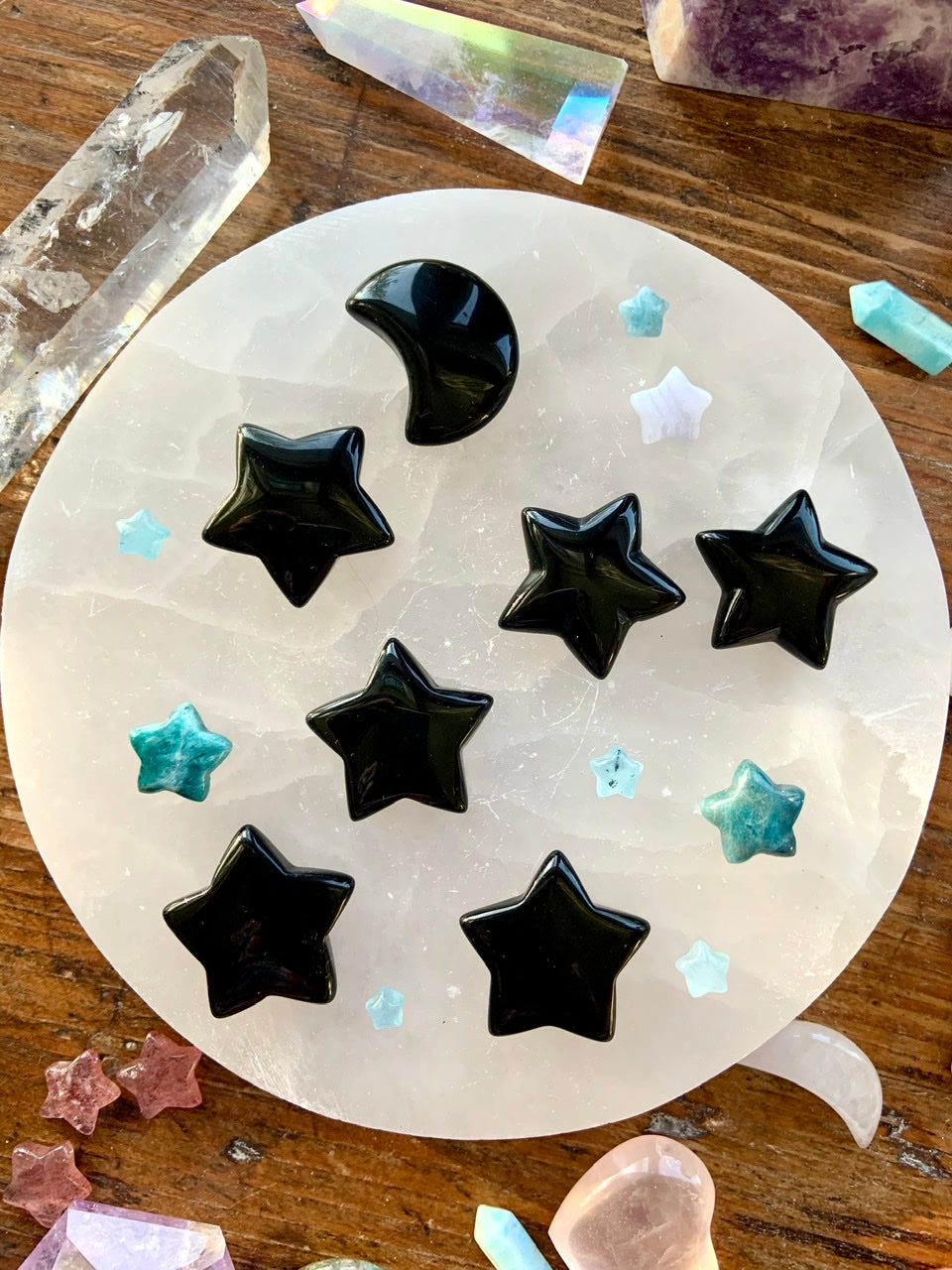 Overhead view of Black Obsidian moons and stars on a white selenite charging plate — polished crystal carvings for protection, grounding, and energy clearing