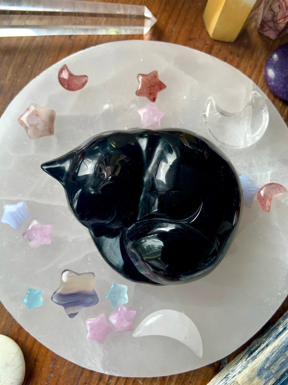 Overhead shot of sleeping Black Obsidian cat on selenite plate with pastel celestial crystals — soothing crystal keepsake for protection & healing.