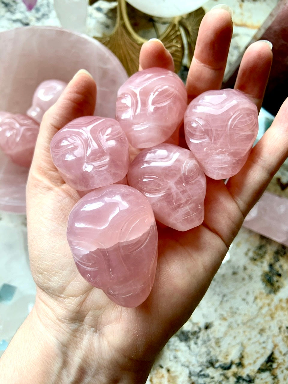 Hand holding five carved Rose Quartz alien heads – crystal carvings for love, heart chakra healing + cosmic energy