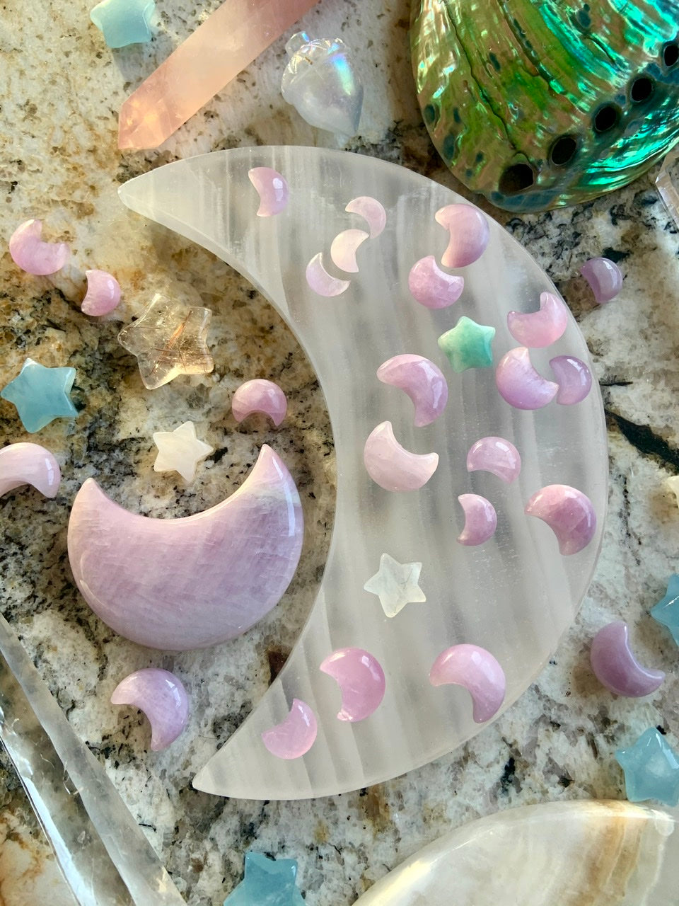 Overhead image of Kunzite moons on a white moon plate with a large Kunzite moon & surrounding crystals — tools for lunar magic & healing intention.