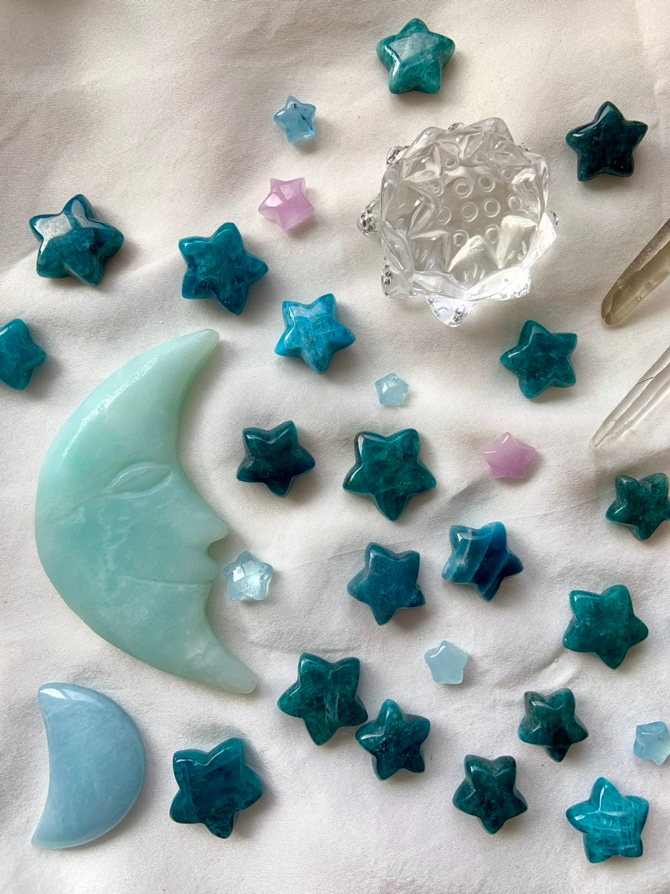 Cosmic crystal arrangement with Blue Apatite stars, aquamarine moons, kunzite stars & quartz lotus carving — dreamy Throat Chakra display on white silk.