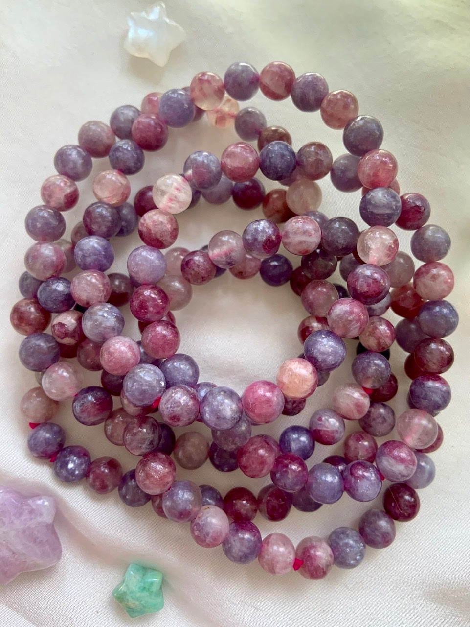 Stack of Unicorn Stone crystal bracelets on white silk — Pink Tourmaline in Lepidolite beaded jewelry with celestial crystals for emotional healing + divine support.
