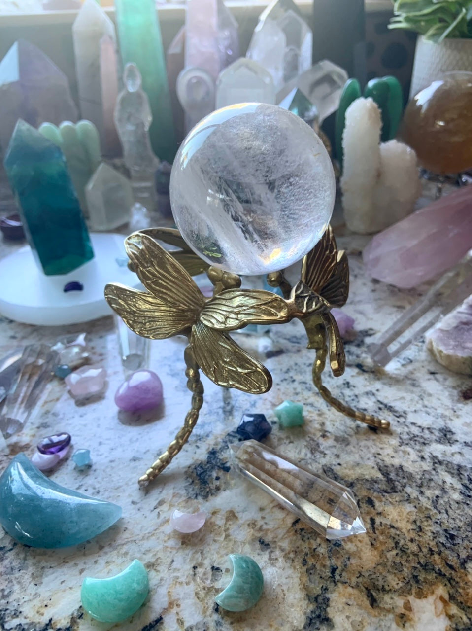 Gold dragonfly sphere stand displaying a clear quartz crystal ball in the midst of a colorful crystal collection.