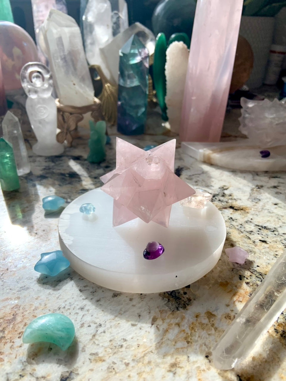 Round selenite plate as a display base for large rose quartz merkaba carving, styled within crystal collection