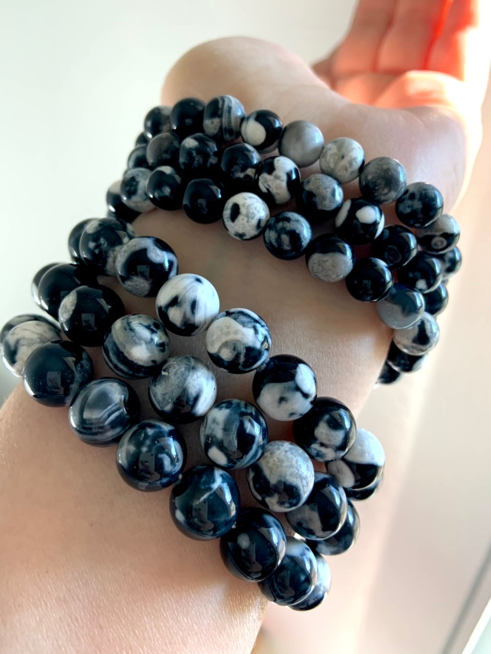 Stack of six Orca Agate bracelets separated into two bead size groups — 10–11mm and 8–9mm — worn on wrist for size comparison