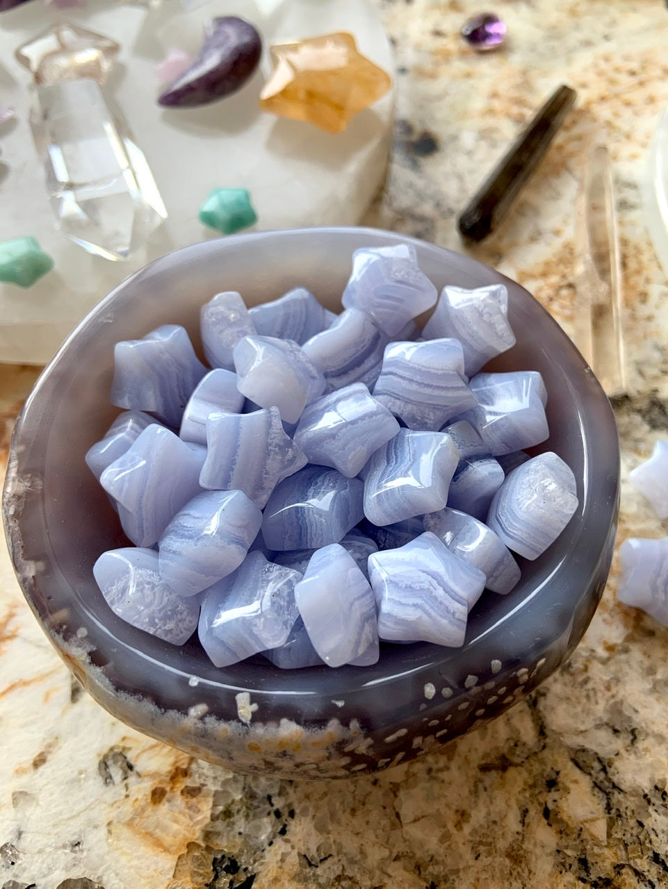 Close-up of Blue Lace Agate stars in an agate bowl with crystal grid in background — serene Throat Chakra stones for sacred space rituals.