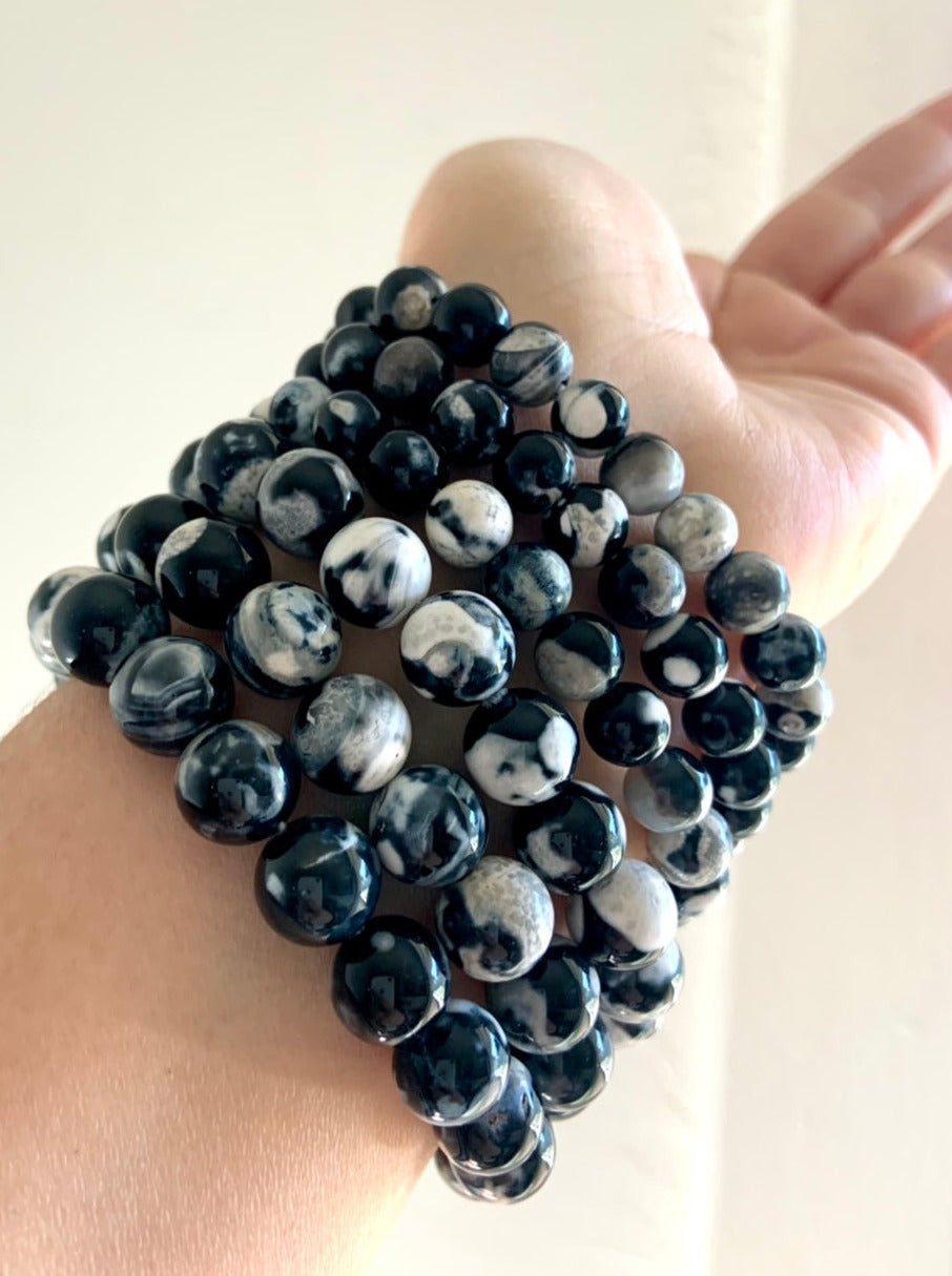 Orca Agate crystal bracelets worn in a stacked set on wrist showing three different bead sizes: 10–11mm, 8–9mm, and 6–7mm