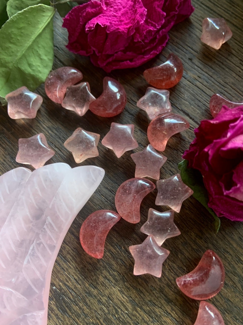 Strawberry Quartz moons and stars on dark wood with red roses and rose quartz angel wing carving — mini tanzberry crystal carvings for heart healing and joy