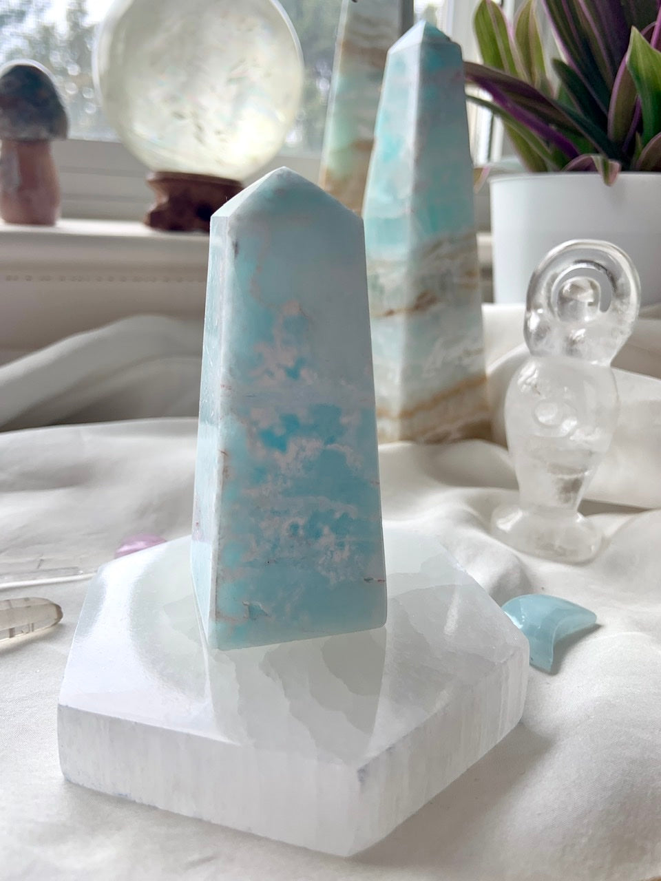 Lifestyle display of selenite hexagon plate holding a Caribbean calcite tower, surrounded by crystals in sacred space décor