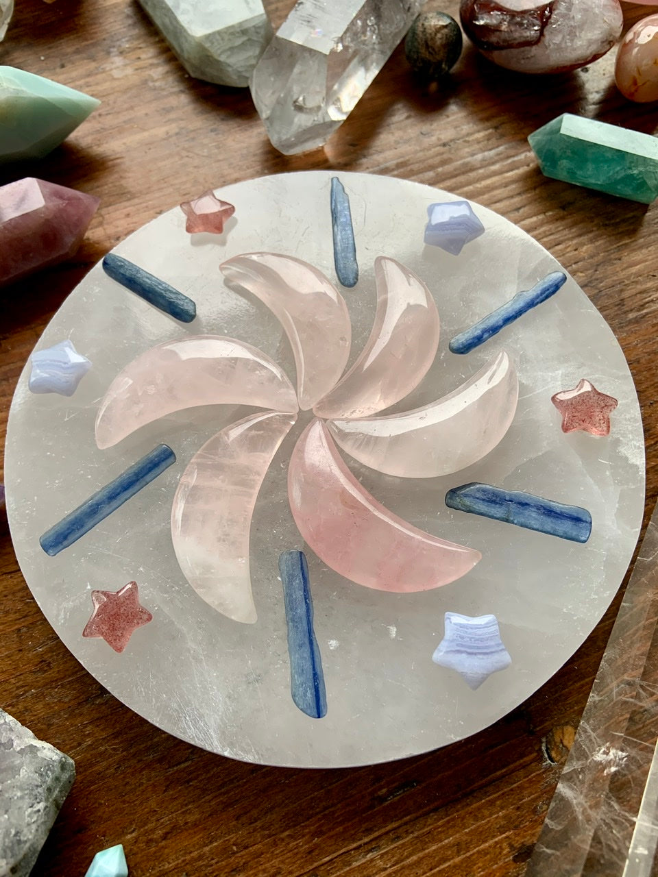 Crystal grid with Strawberry Quartz stars, Rose Quartz moons, Kyanite sticks, and Blue Lace Agate stars on wood table with additional healing crystals