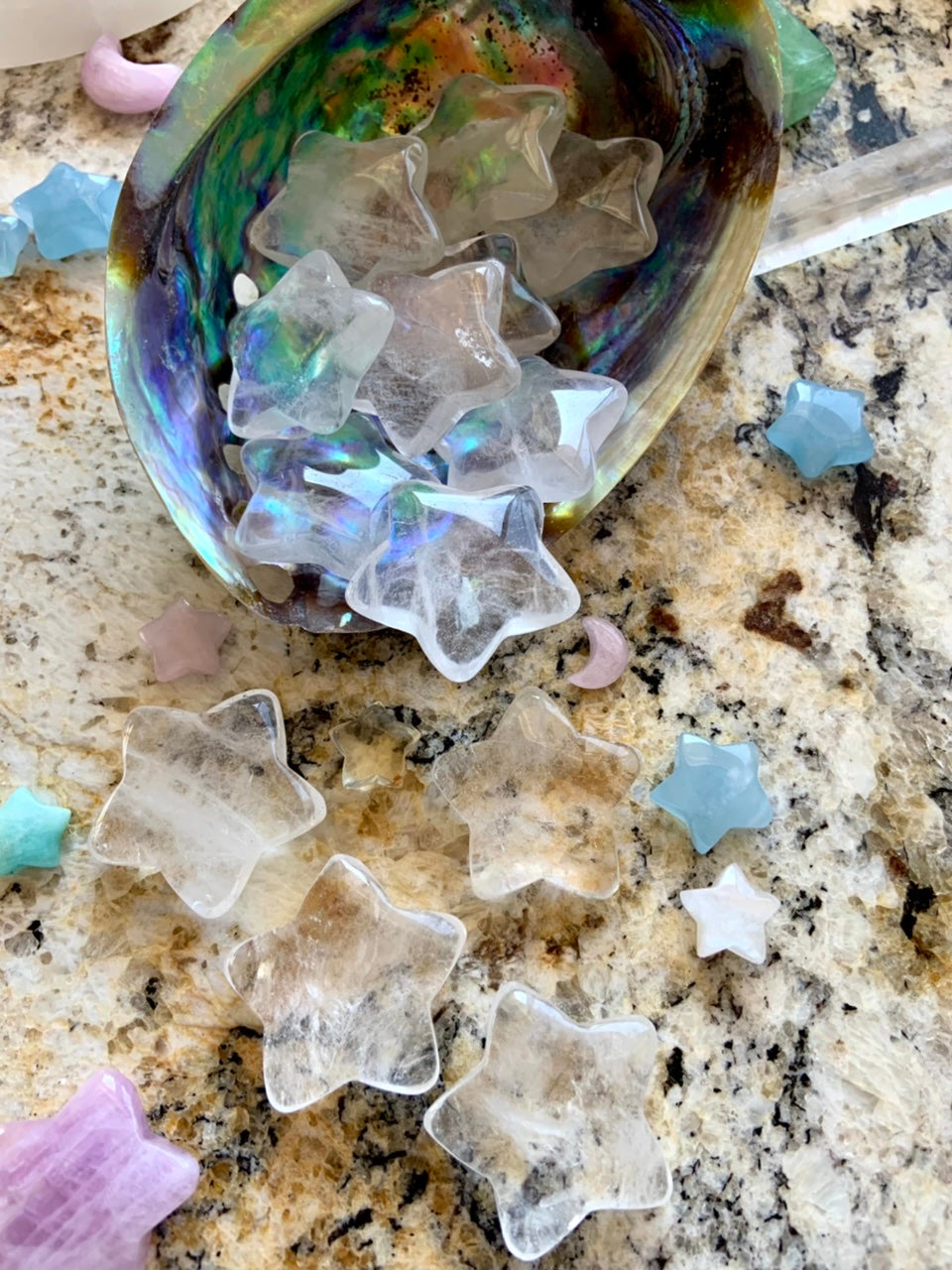 Wide angle view of Clear Quartz stars spilling from abalone shell onto granite surface, celestial crystals for chakra healing and altar décor