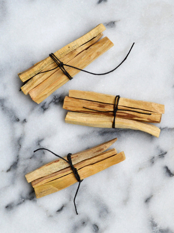 Ethically Harvested Palo Santo Sticks from Ecuador in Bundles of three sticks tied with black hemp twine shown on a marble background