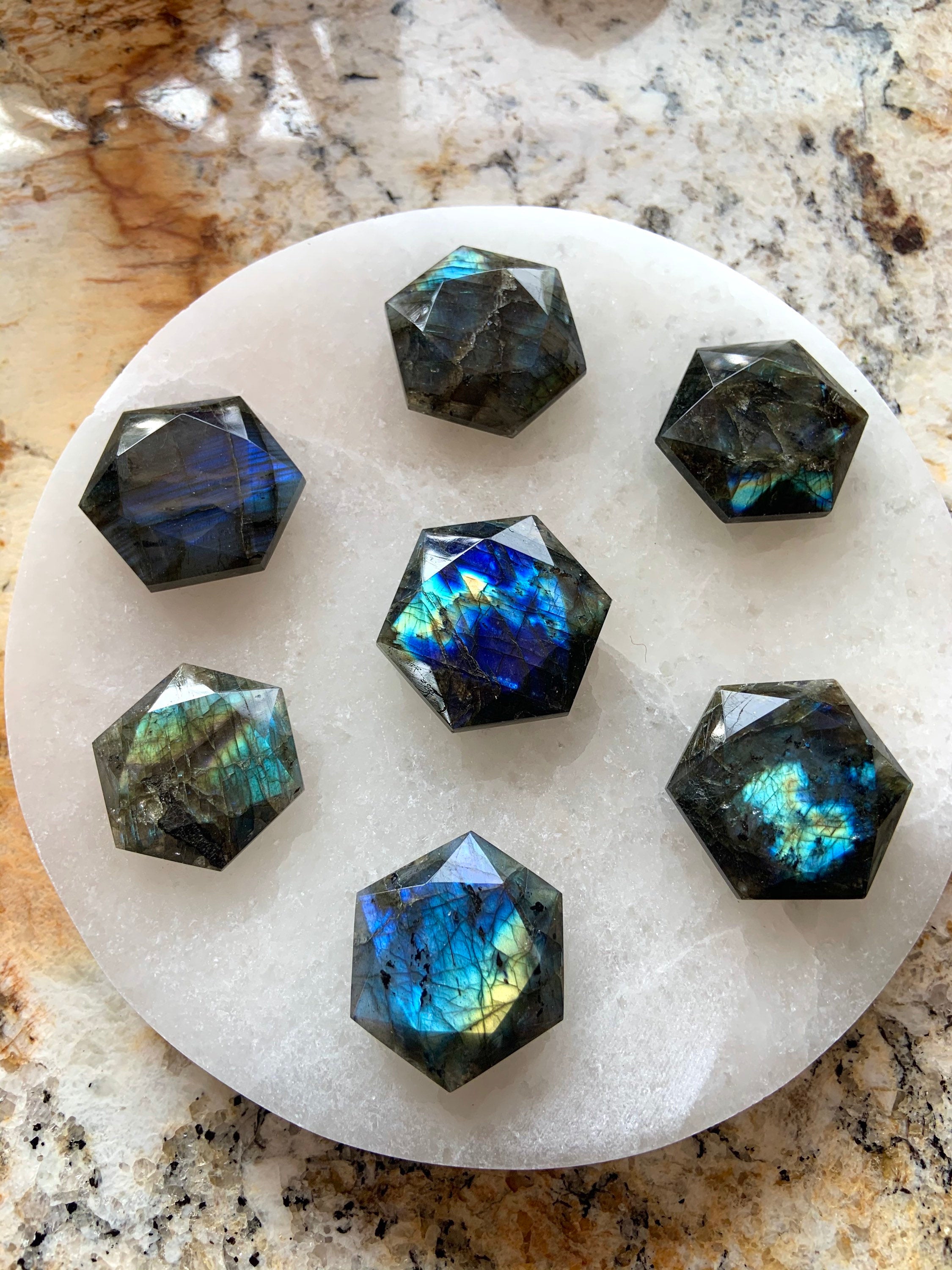 Seven flashy Labradorite hexagons arranged on a crystal grid atop a white selenite plate — powerful Third Eye activation stones for spiritual energy work.
